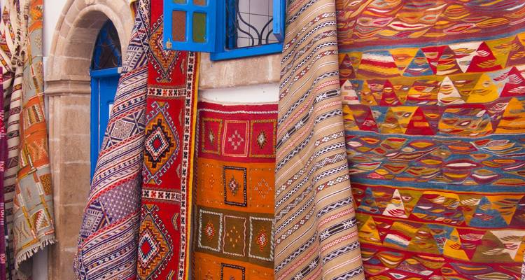 Tapis berbères tissés à la main colorés suspendus à l'extérieur d'une boutique en pierre avec des fenêtres bleu vif.