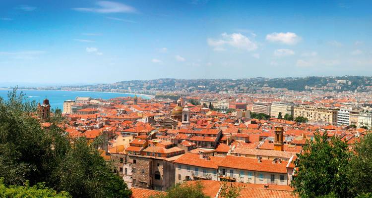 Vue panoramique d'une ville côtière aux toits de tuiles rouges.