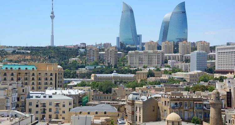 Stadtlandschaft mit modernen Wolkenkratzern, einschließlich ikonischer flammenartiger Türme, vor einer Hügelkulisse.