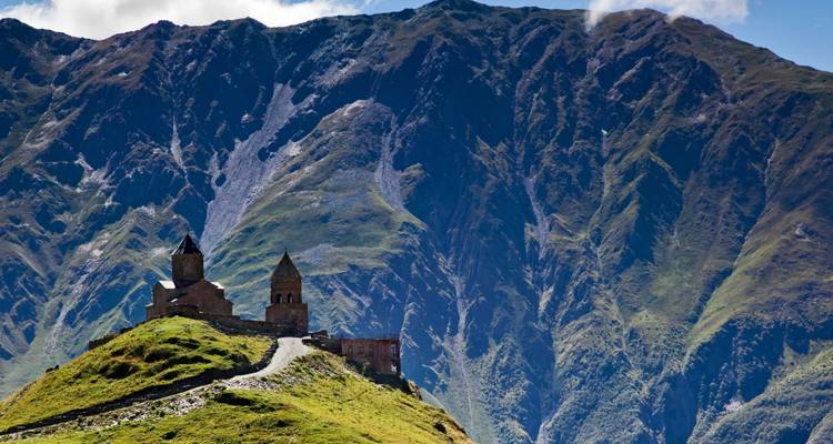 Rustikaler Berghang mit einer kleinen Kirche und nebligem Gebirgshintergrund.