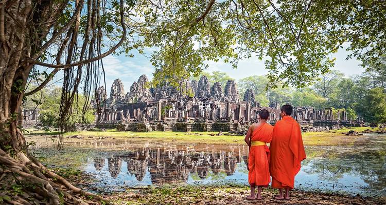 Deux moines en robes orange se tenant près d'un temple se reflétant dans un étang.