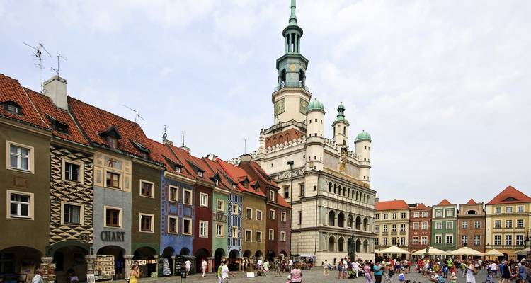 A colorful historic square with a clock tower and bustling activity.