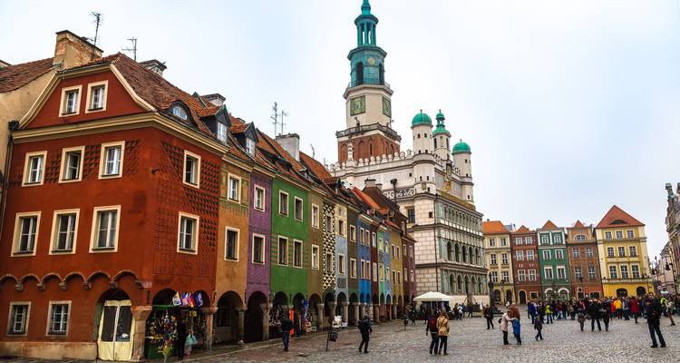 Casas históricas de colores vivos y el Ayuntamiento renacentista de Poznan dominando una plaza empedrada llena de peatones.