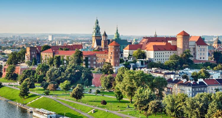 Panoramic view of a historic castle complex with red roofs and a river.