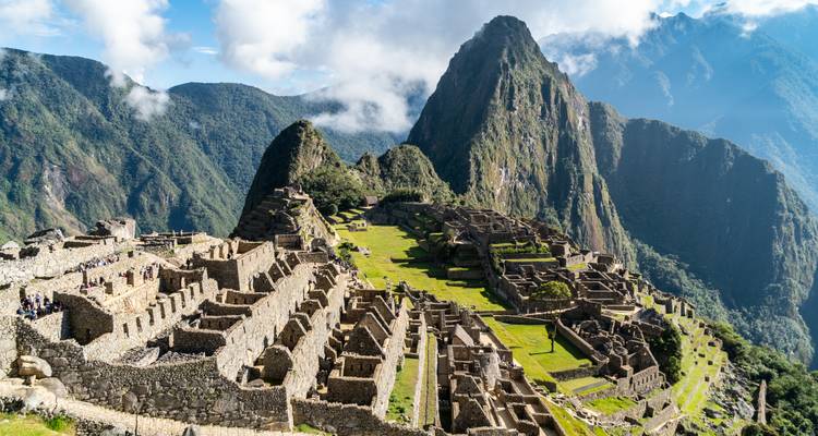 Vue emblématique sur les ruines en terrasses du Machu Picchu se détachant contre les pics luxuriants des Andes et les nuages.