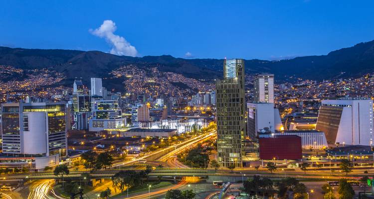 Nachtelijk panorama van Medellín's moderne skyline met verlichte gebouwen en kronkelende verkeerssporen.