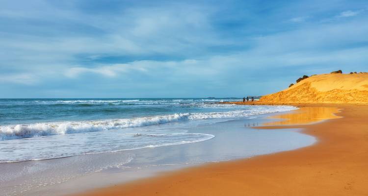Sandy beach with waves and clear sky.