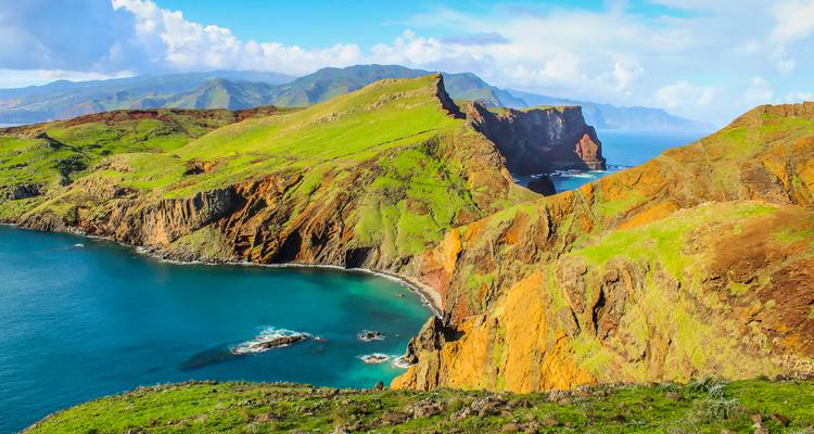 Acantilados volcánicos de un verde y naranja vibrantes que se despeñan en las aguas turquesas del Atlántico en la costa accidentada de Madeira.