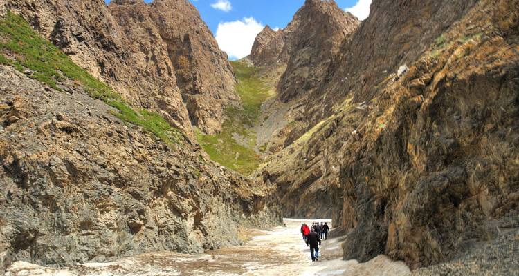 Kleine Wandergruppe geht durch eine schmale, schattige Schlucht mit steilen Felswänden und Schneeflecken