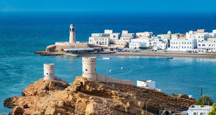 Surs Küstenwachtürme und weiße Gebäude neben dem blauen Oman-Meer an einem sonnigen Tag.