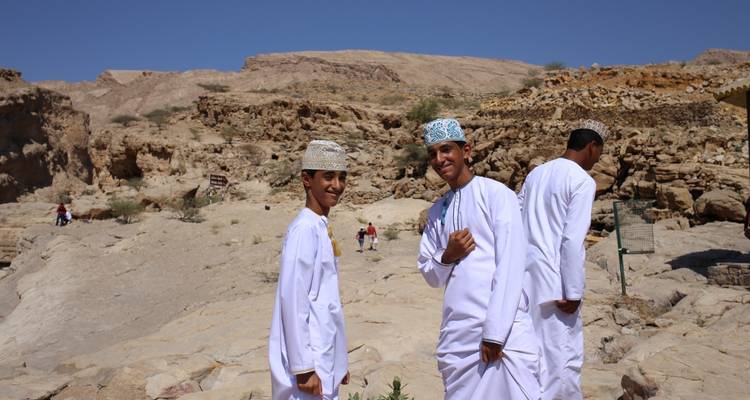 Drie mannen in traditionele Omaanse kledij poseren in een rotsachtige buitenomgeving.