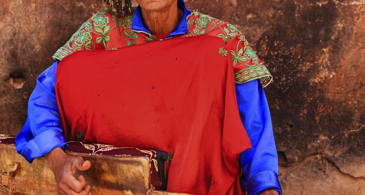 Portret van een persoon in traditionele kleurrijke kleding in een rustieke omgeving.