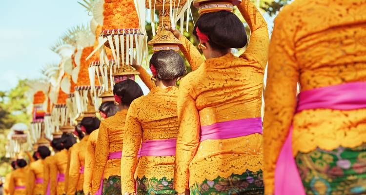 Procession of women in traditional attire carrying offerings on their heads.
