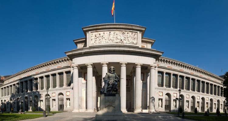 Neoklassizistische Fassade des Prado-Museums in Madrid unter einem tiefblauen Himmel mit wehender spanischer Flagge.