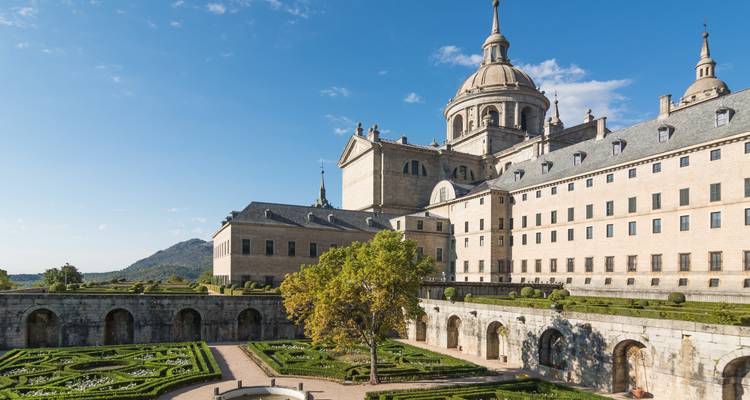 Majestätischer Klosterkomplex El Escorial mit gepflegten Gärten und Bergkulisse unter klarem Himmel.