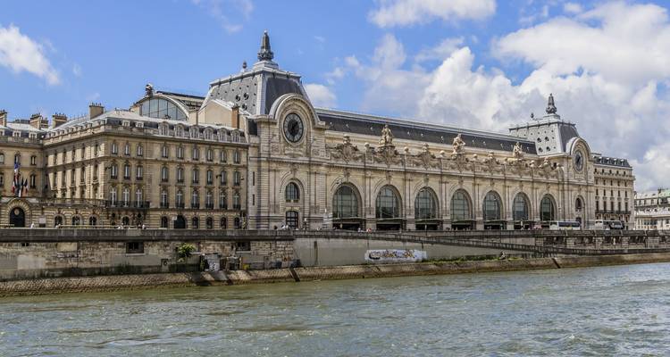 Große Fassade des Musée d'Orsay entlang der Seine unter vereinzelten Wolken.