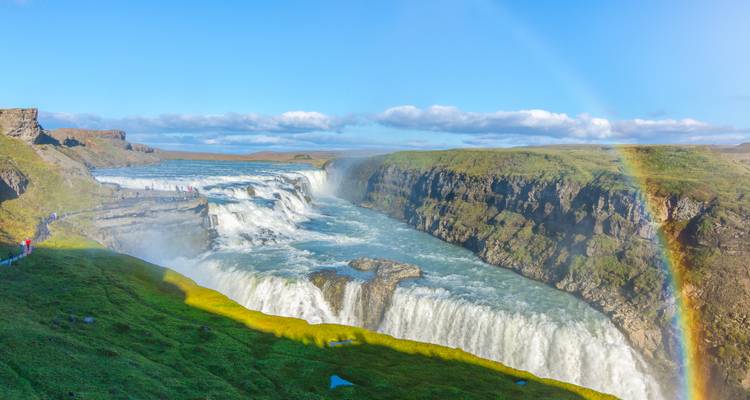 Der mächtige Gullfoss-Wasserfall stürzt in einen Canyon mit grünen moosigen Felswänden und einem strahlenden Regenbogen.