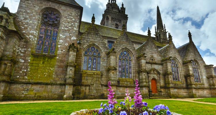 Église gothique ornée avec des arcs-boutants, des vitraux et un parterre de fleurs en fleurs devant.
