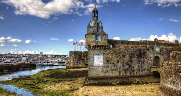 Remparts de pierre et tour de l'horloge de la ville fortifiée de Concarneau surplombant le port à marée basse.