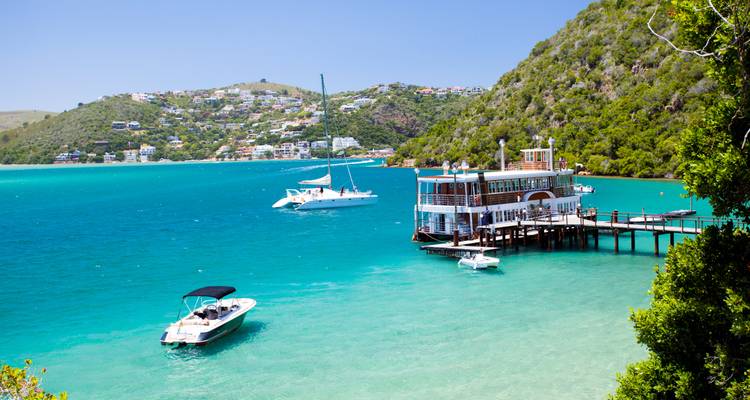Barcos turísticos en una bahía turquesa con un muelle y casas en la ladera.