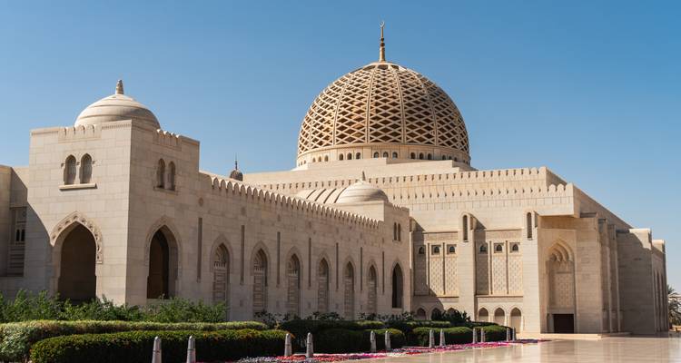 Gran mezquita de mármol blanco con cúpula de celosía intrincada contra un cielo azul claro.