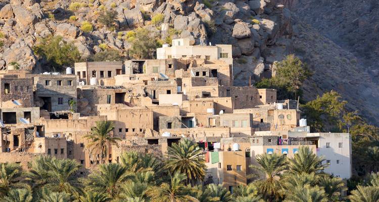 Pueblo de montaña tradicional de ladrillos de barro enclavado contra acantilados rocosos con palmares abajo.