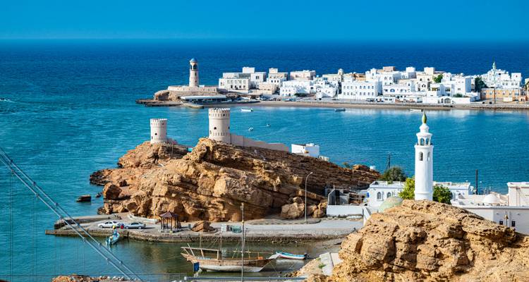 Ciudad costera con torres de vigilancia gemelas y edificios blancos con vista a una bahía turquesa serena.