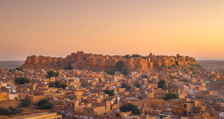 Golden-hued desert fort rises above the sandstone rooftops of Jaisalmer at sunset.