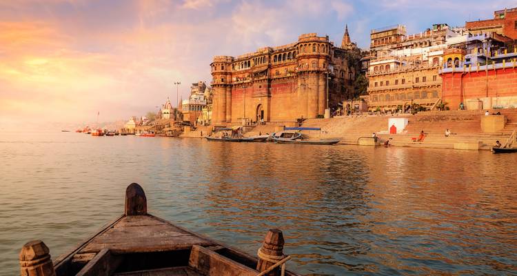 Boat glides on the Ganges beside the ancient ghats of Varanasi at golden sunset.