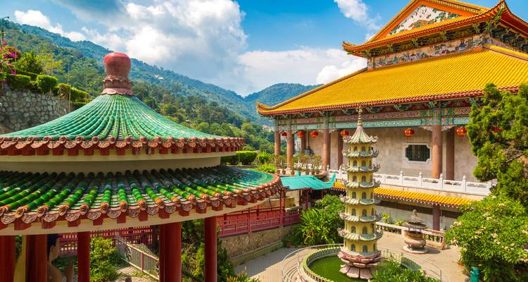 Prachtvoller chinesischer Tempelkomplex mit bunten Dächern vor üppig grünen Hügeln und blauem Himmel
