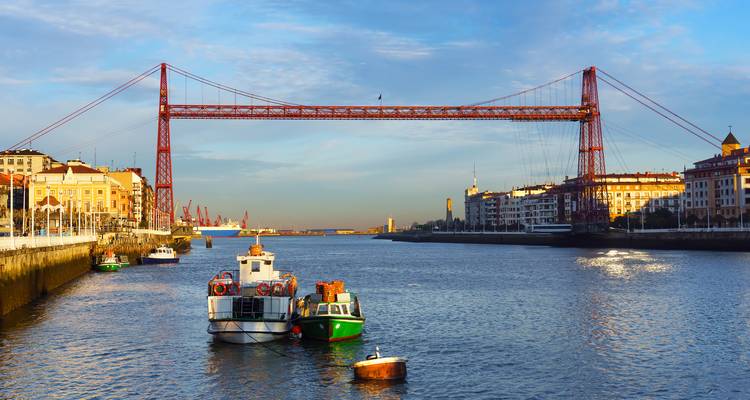 Puente Colgante de Vizcaya atravesando el río Nervión con pequeños barcos amarrados debajo bajo la luz de la madrugada.