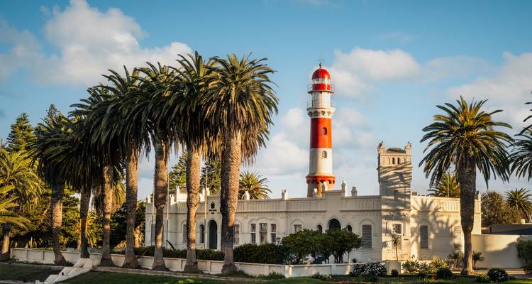 Phare historique avec palmiers sous un ciel bleu dégagé.