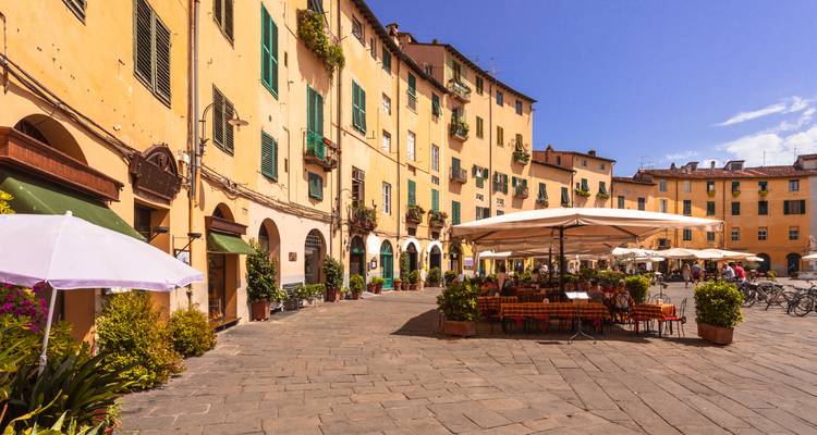 Charmante piazza ovale bordée de bâtiments médiévaux jaunes et de cafés en terrasse dans Lucques baignée de soleil.