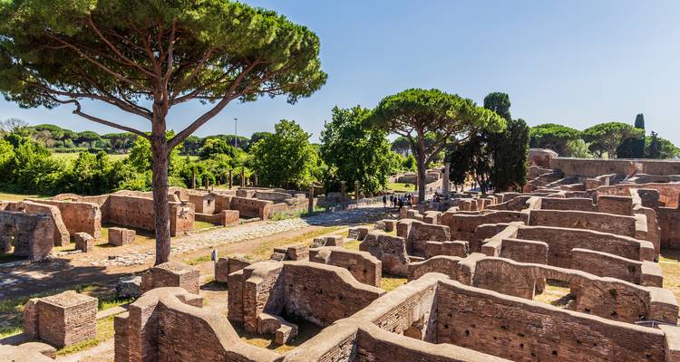 Ausgedehnte Backsteinruinen der antiken Hafenstadt Ostia Antica, beschattet von hohen Pinien.