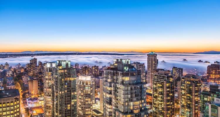 Horizonte del amanecer de Vancouver con torres emergiendo sobre un mar de niebla y montañas distantes.