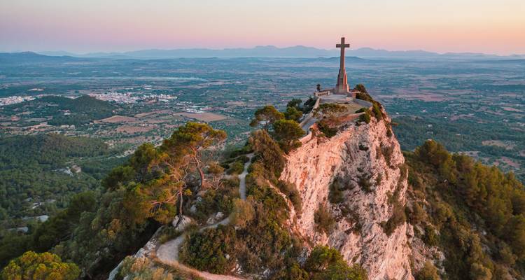 Hilltop cross monument overlooking a vast valley and distant mountain range at sunrise