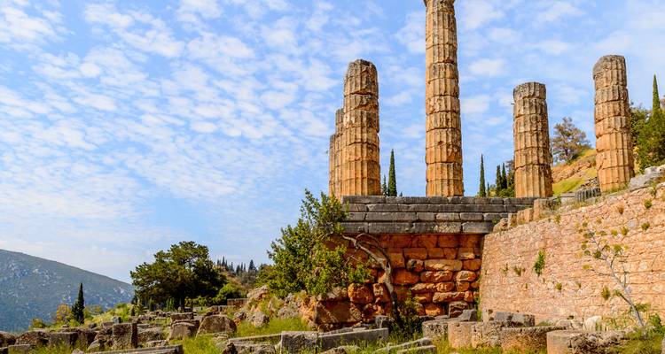 Verfallene Steinsäulen des Apollo-Tempels stehen vor der Kulisse des Berges Parnass und blauem Himmel.