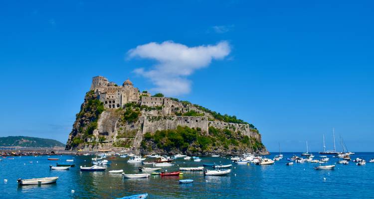 Het Aragonese Kasteel rijst majestueus op vanaf een rotsachtig eilandje omringd door aangemeerde boten voor de kust van Ischia.