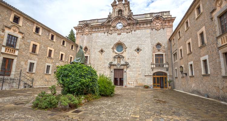 Patio de piedra frente a una fachada de monasterio ornamentado coronada con una torre reloj