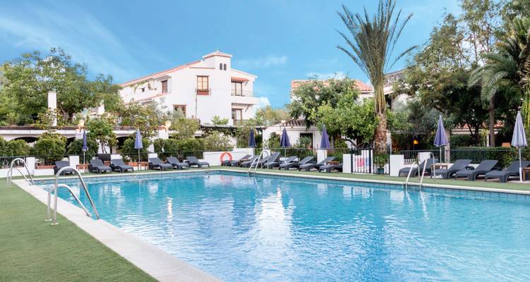Resort mit einem Schwimmbad und Liegestühlen unter blauem Himmel.