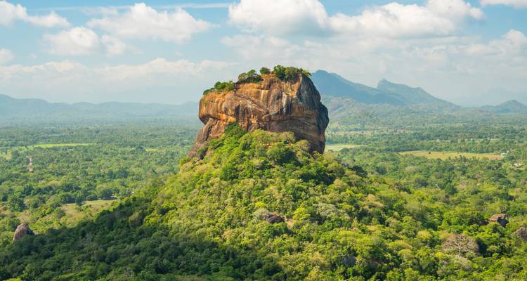 Icónica fortaleza rocosa de Sigiriya elevándose sobre un denso bosque verde bajo nubes blancas esponjosas