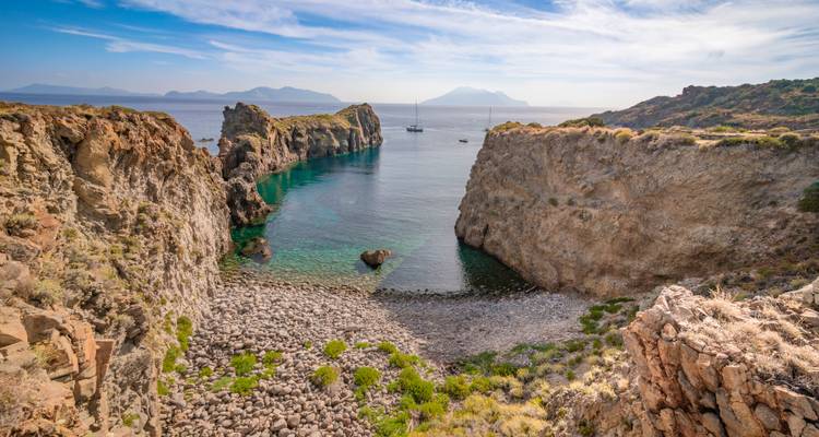 Heldere turkooizen baai tussen ruige vulkanische rotsen met zeilboten voor anker