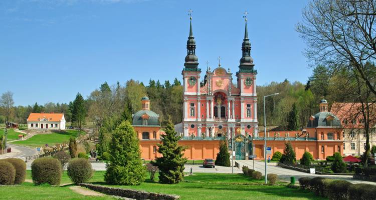 Barockkirche mit Zwiebeldächern und zwei schwarzen Türmen, die sich über gepflegtem Gelände unter klarem blauen Himmel erheben.