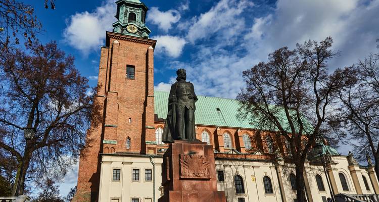 Statue vor der Posener Kathedrale mit einem Backsteinturm und blauem Himmel.