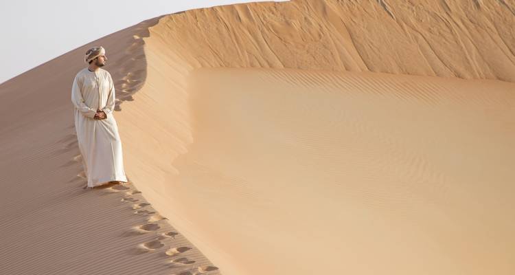 Mann in traditioneller omanischer Kleidung, der auf einer Sanddüne steht.