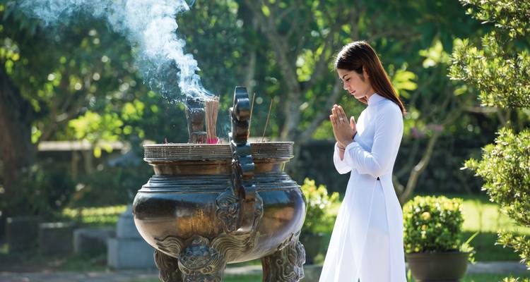 Vrouw die bidt bij een wierookaltaar in een tuin.