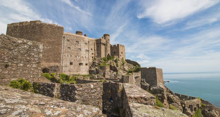 Un castillo de piedra medieval se alza en la cima de un acantilado costero rocoso que domina el mar