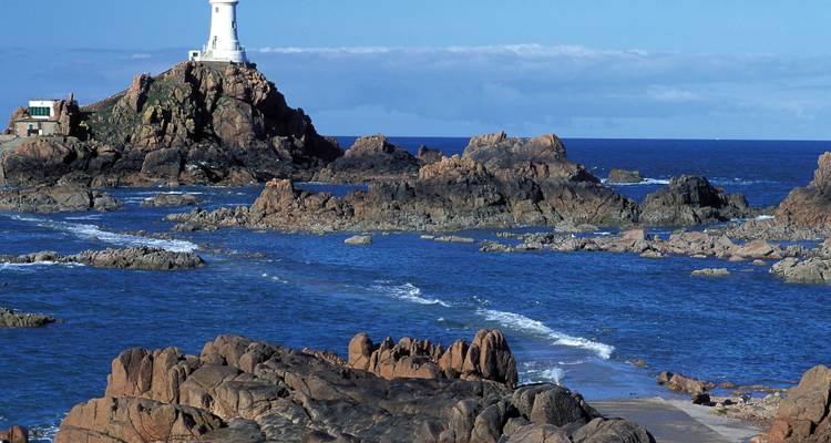 Phare sur côte rocheuse avec ciel bleu.