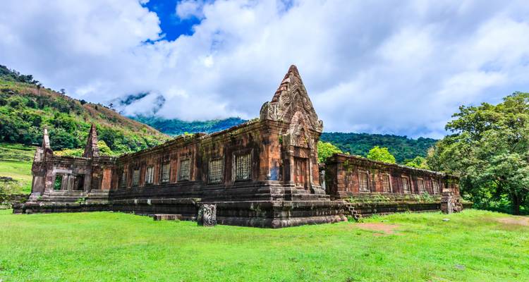 Alter Sandstein-Tempelkomplex vor nebligen bewaldeten Hügeln unter einem hellen Himmel.