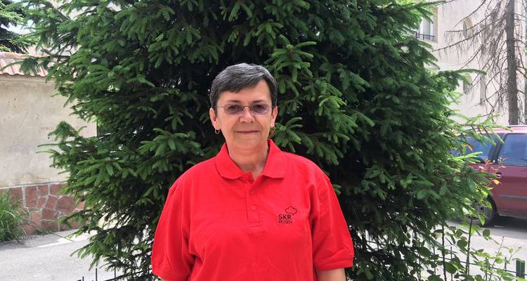 Person posiert vor einem üppig grünen Baum.